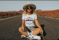 Thumbnail for a woman sitting on the side of a road wearing a cowboy hat