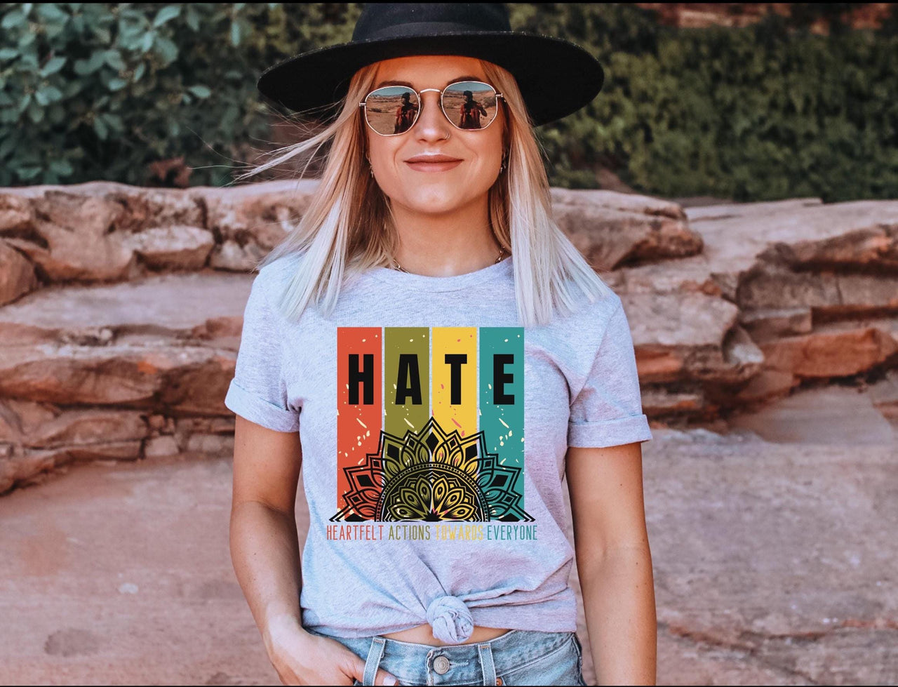 a woman wearing a hat and sunglasses standing in front of a rock wall