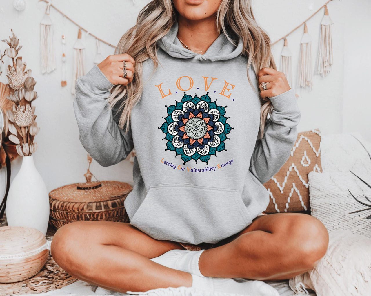 a woman sitting on a bed wearing a grey love hoodie