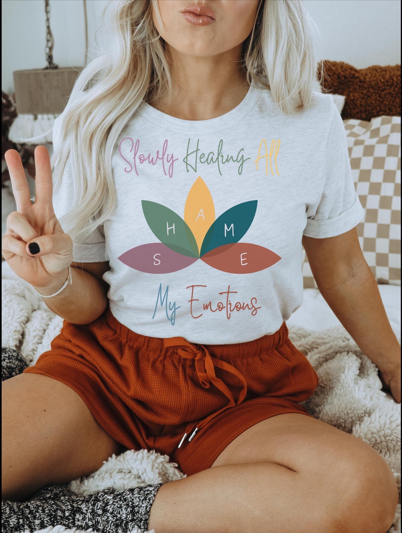 a woman sitting on top of a bed holding a peace sign