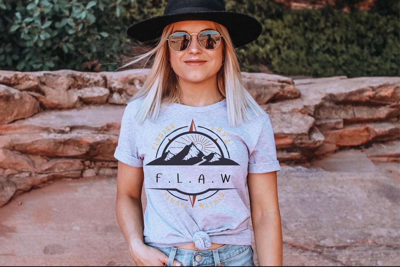 a woman wearing a hat and sunglasses standing in front of a rock wall