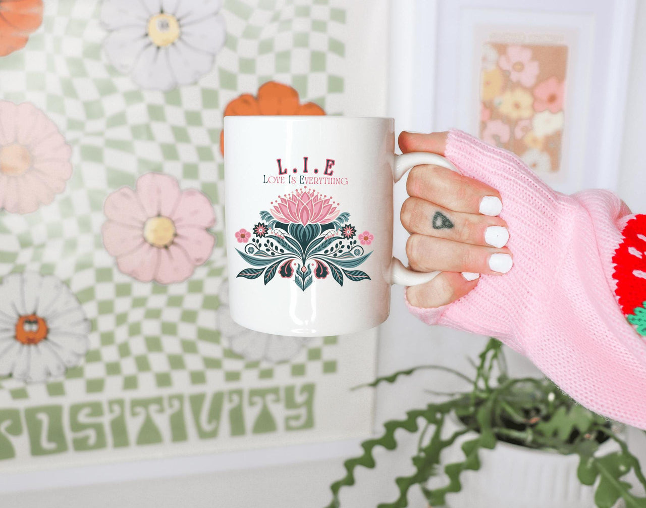 a woman's hand holding a coffee mug in front of a wall with flowers